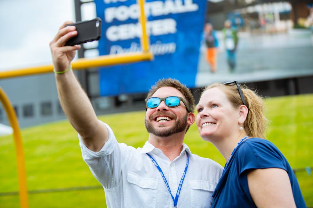 Two guests taking a selfie on the field at the Jamie Hosford Football Center dedication.